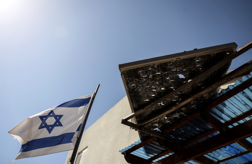 An Israeli national flag is seen next to a damaged part of a roof following rockets that were launched from the Gaza Strip, in Sderot, Israel May 10, 2023 (photo credit: REUTERS/AMMAR AWAD)