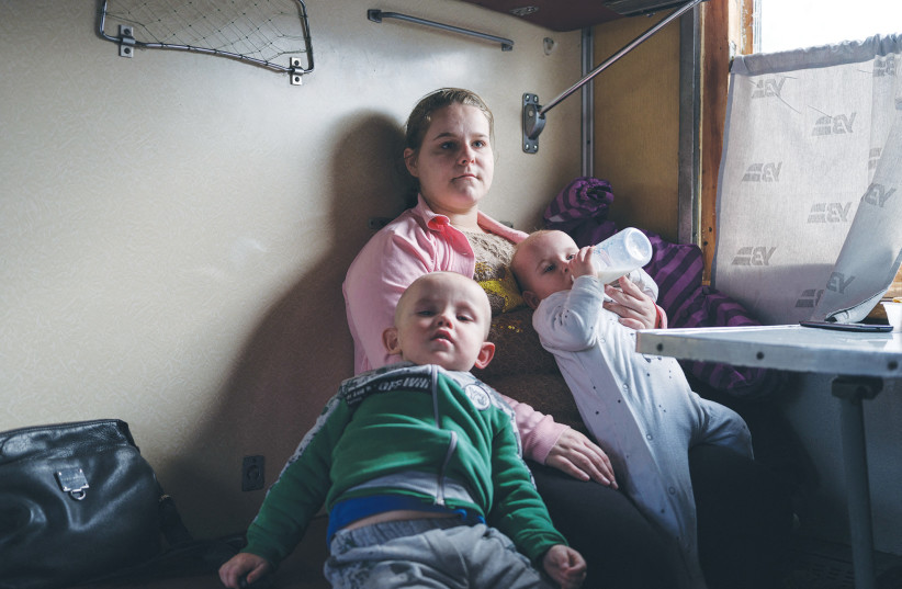  A WOMAN sits with her two small children aboard an evacuation train after leaving their frontline village in Donetsk region, Ukraine. Among all the civilian challenges, children are the priority.  (photo credit: MARKO DJURICA/REUTERS)