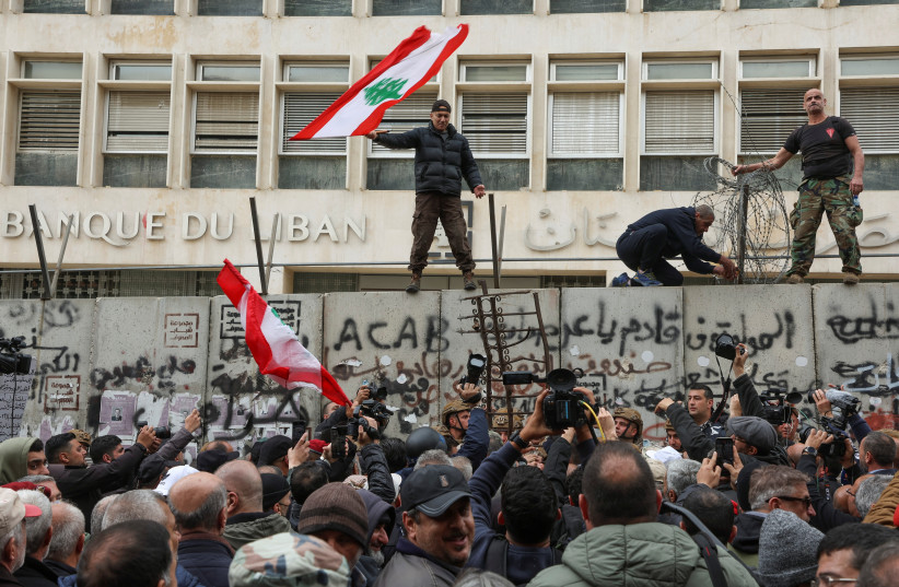  A demonstrator holds the Lebanese flag as he stands on a barricade during a protest over the deteriorating economic situation in front of the Central Bank building in Beirut, Lebanon March 30, 2023. (photo credit: REUTERS/MOHAMED AZAKIR)
