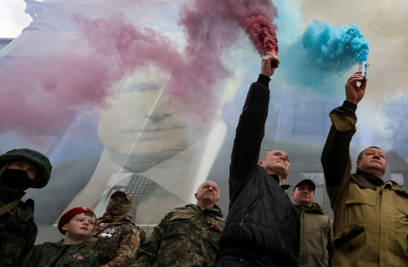 Participants burn flares in front of a banner with a portrait of Russian President Vladimir Putin during a patriotic flash mob marking the ninth anniversary of Russia's annexation of Crimea, in Yalta, Crimea March 17, 2023. (credit: REUTERS/ALEXEY PAVLISHAK)