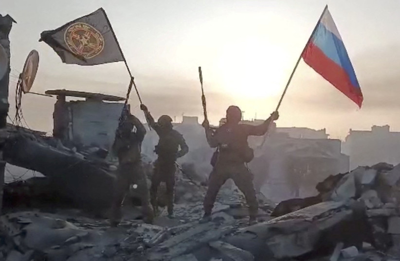 Wagner mercenary group fighters wave flags of Russia and Wagner group on top of a building in an unidentified location, in the course of the Russia-Ukraine conflict, in this still image obtained from a video released on May 20, 2023.