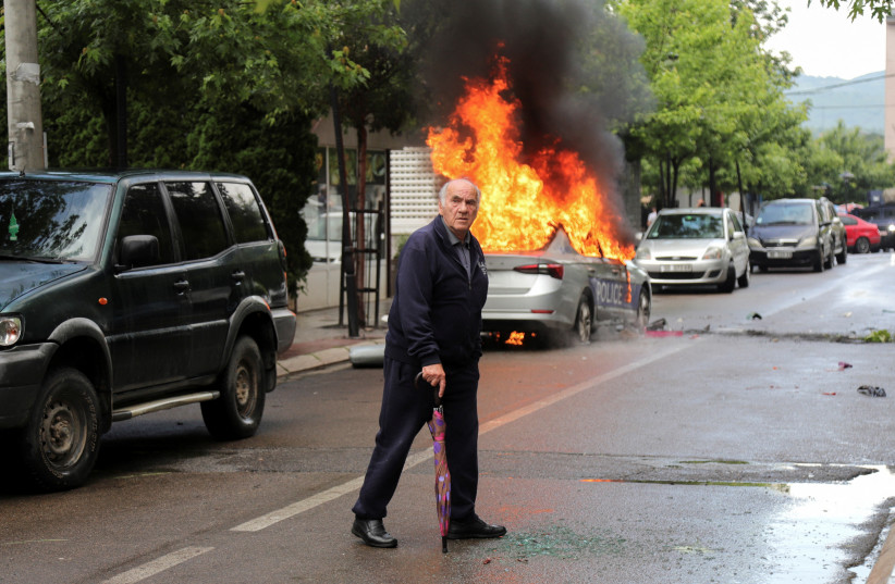 A man walks past a burning police car, during clashes between Kosovo police and ethnic Serb protesters, who tried to prevent a newly-elected ethnic Albanian mayor from entering his office, in the town of Zvecan, Kosovo, May 26, 2023 (credit: REUTERS/Miodrag Draskic)
