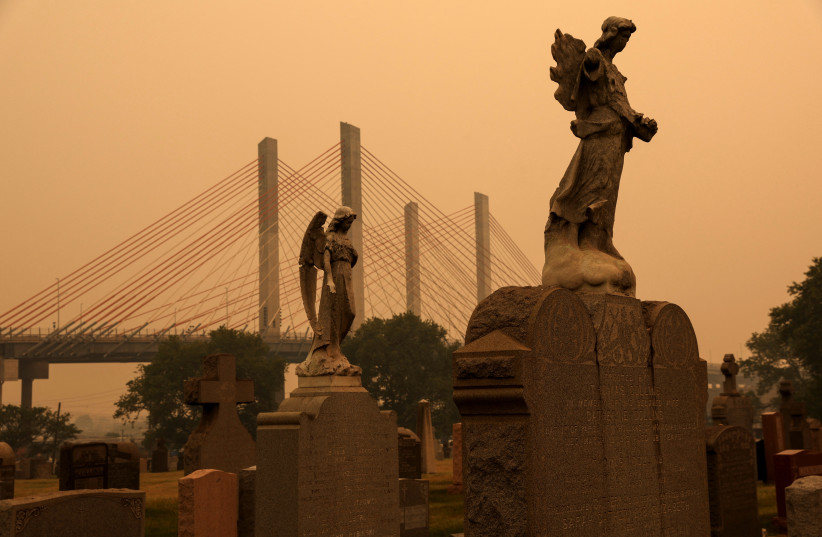  The head of a tombstone is seen as haze and smoke from the Canadian wildfires shroud the sky at the Calvary Cemetery in the Queens Borough of New York City, US, June 7, 2023. (credit: Shannon Stapleton/Reuters)