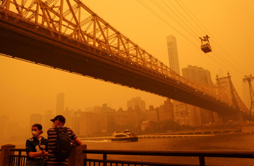  People wear protective masks as the Roosevelt Island Tram crosses the East River while haze and smoke from the Canadian wildfires shroud the Manhattan skyline in the Queens Borough New York City, US, June 7, 2023. (credit: Shannon Stapleton/Reuters)