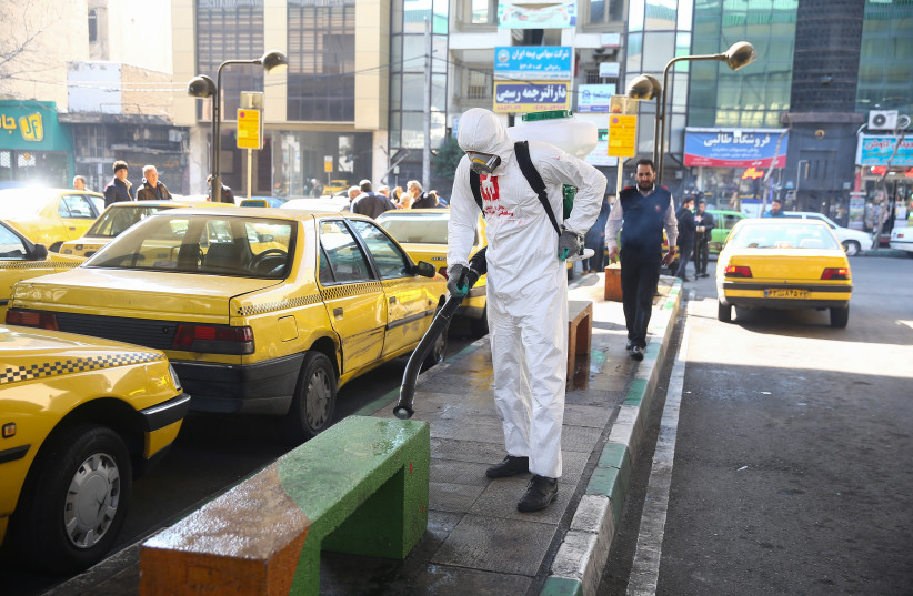 A member of the medical team wears a protective face mask, following the coronavirus outbreak, as he sprays disinfectant liquid to sanitise a taxi station in Tehran, Iran March 05, 2020 (credit: WANA (WEST ASIA NEWS AGENCY)/NAZANIN TABATABAEE VIA REUTERS)