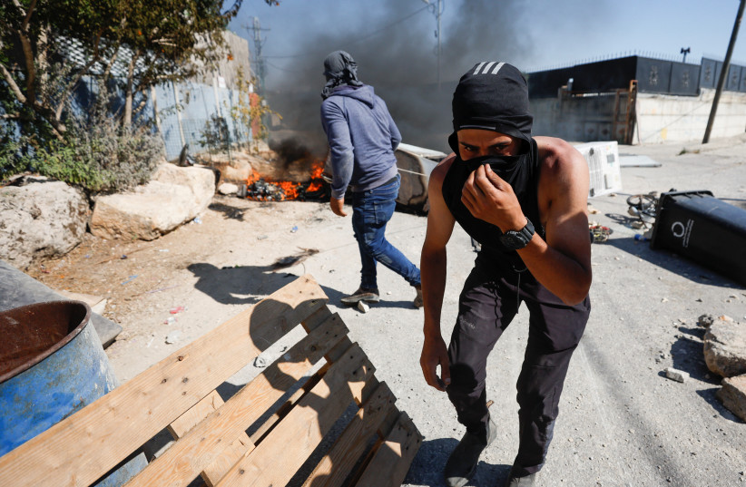 A Palestinian covers his face during clashes with Israeli troops after Israeli settlers attack Umm Safa village near Ramallah, in the West Bank, June 24, 2023 (credit: REUTERS/MOHAMAD TOROKMAN)