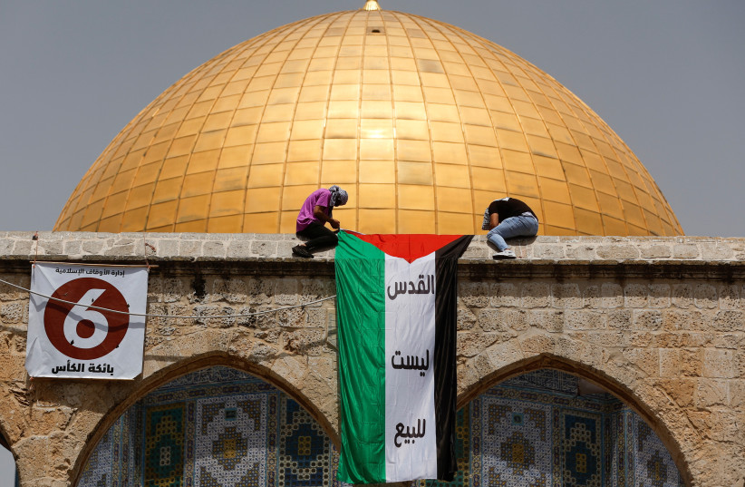  Palestinians mount a national flag in a protest on the last Friday of Ramadan ahead of the prayer in front of the Dome of the Rock, in the compound known to Muslims as Noble Sanctuary and to Jews as Temple Mount, in Jerusalem's Old City April 29, 2022. (credit: AMMAR AWAD/REUTERS)