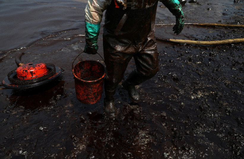 A worker cleans up an oil spill following an underwater volcanic eruption in Tonga, in Ancon, Peru January 25, 2022.  (credit: REUTERS/PILAR OLIVARES)