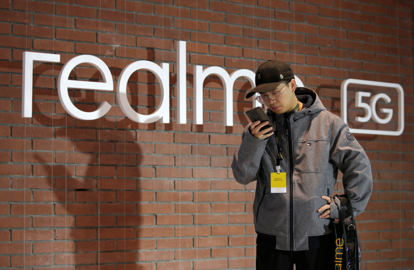  A man looks at his mobile phone next to a logo of Realme during its X50 5G product launch event in Beijing, China January 7, 2020. (credit: REUTERS/JASON LEE)