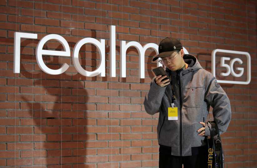 A man looks at his mobile phone next to a logo of Realme during its X50 5G product launch event in Beijing, China January 7, 2020.