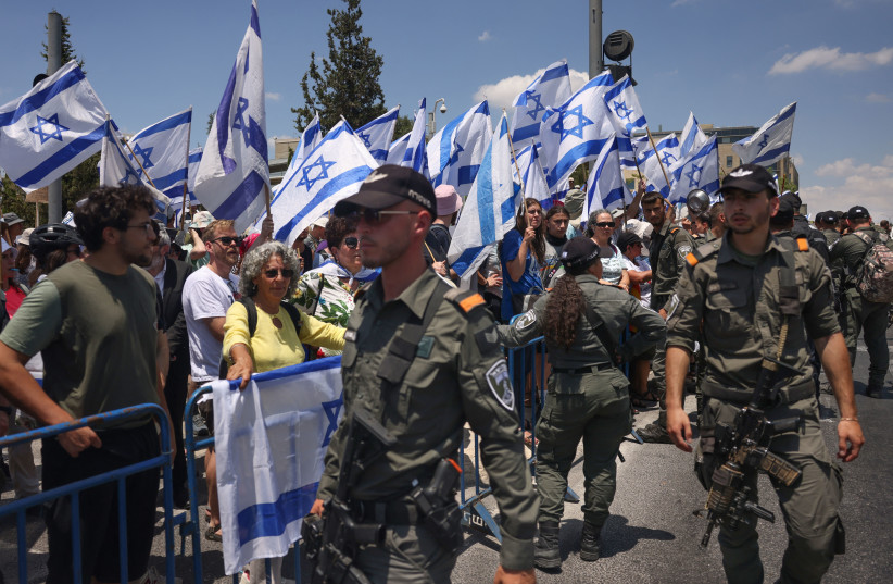  Israeli security forces stand guard in front of protesters waving national flags near the Parliament in Jerusalem, on July 11, 2023. (credit: Menahem Kahana/AFP via Getty Images)