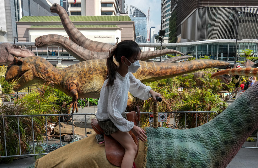 A girl rides on a dinosaur statue during Children's Day celebration at a department store in Bangkok, Thailand, January 14, 2023.  (credit: ATHIT PERAWONGMETHA / REUTERS)