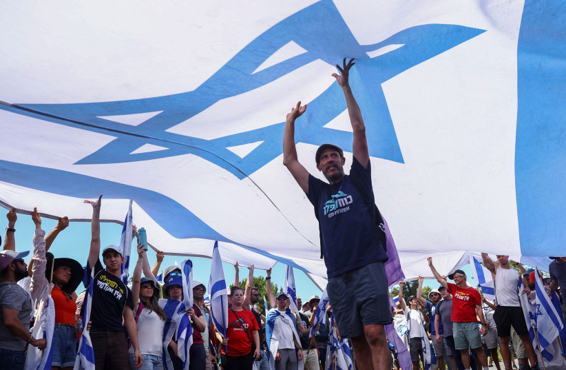  Protesters hold up a large Israeli flag at a demonstration following a parliament vote on a contested bill that limits Supreme Court powers to void some government decisions, in Jerusalem July 24, 2023. (credit: REUTERS/Ronen Zvulun)