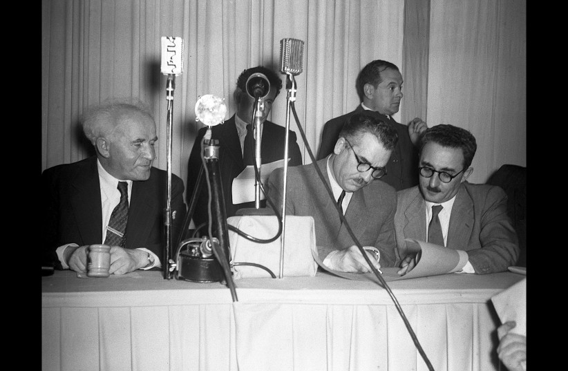  David Ben-Gurion watches Moshe Shapira sign the Declaration of Independence, held by Moshe Sharett, during the signing ceremony at the Tel Aviv Museum on May 14, 1948. (credit: HANS PINN)