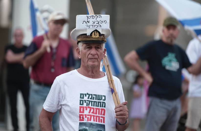  An anti-judicial reform protester wears a hat reading ''the captain is sinking the state'' in front of the home of Knesset Speaker Amir Ohana. (credit: AVSHALOM SASSONI)