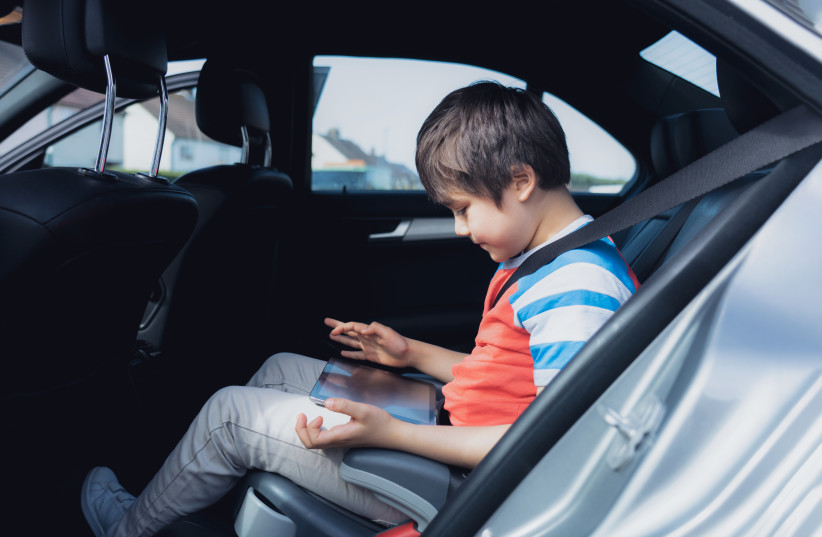  A young child uses a tablet in the back seat of a car (illustrative) (credit: INGIMAGE)
