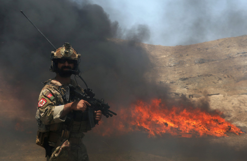  An Afghan police officer keeps watch in front of a pile of burning illegal drugs in the outskirts of Kabul, Afghanistan July 1, 2021. (credit: REUTERS/OMAR SOBHANI)