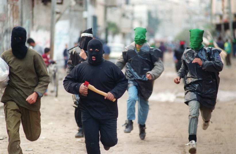  MASKED HAMAS members with axes run through a Gaza street in protest of the Oslo Accords, Dec. 1993 (credit: Fayez Nureldine/AFP via Getty Images)