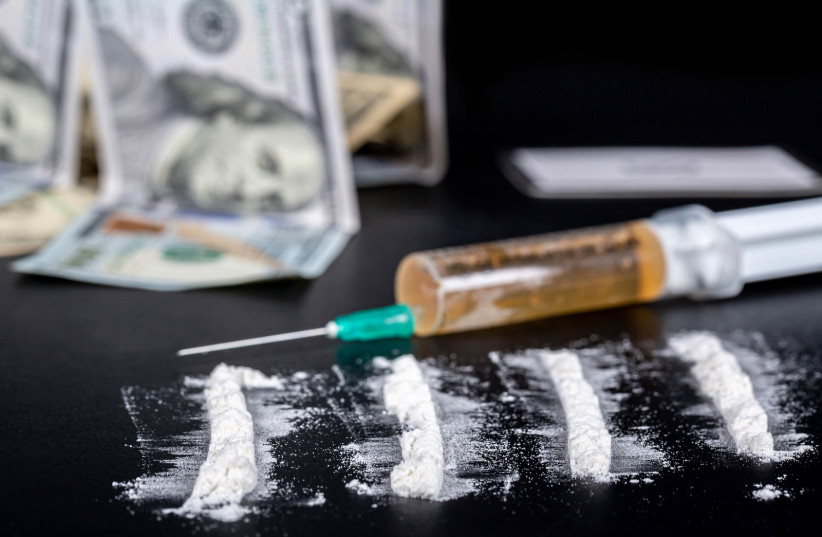  White powder sprinkled on a black background, behind money and a syringe with drugs. (credit: FLICKR)