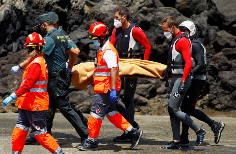  Rescue workers carry the body of a dead person after a boat with 46 migrants from the Maghreb region capsized in the beach of Orzola, in the Canary Island of Lanzarote, Spain June 18, 2021. (credit: REUTERS/BORJA SUAREZ)