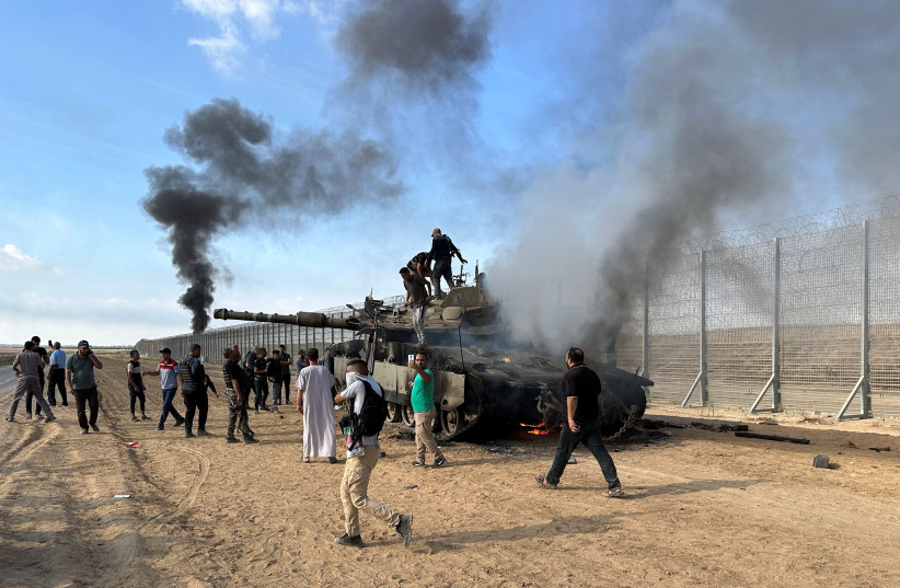  Palestinians react as an Israeli military vehicle burns after it was hit by Palestinian gunmen who infiltrated areas of southern Israel, at the Israeli side of Israel-Gaza border, October 7, 2023.  (credit: REUTERS/Mohammed Fayq Abu Mostafa)