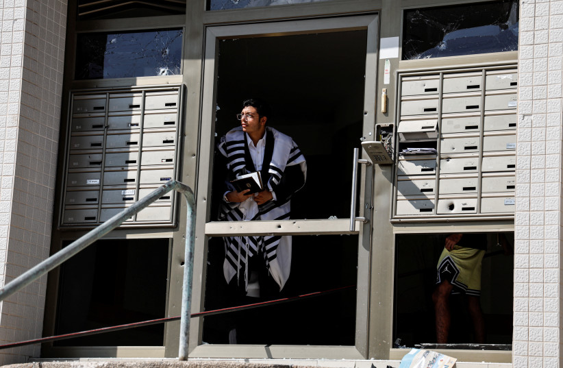  A man wearing a Jewish prayer shawl looks out of the damaged entranceway to a building, as rockets are launched from the Gaza Strip, in Ashkelon, southern Israel October 7, 2023. (credit: REUTERS/AMMAR AWAD)