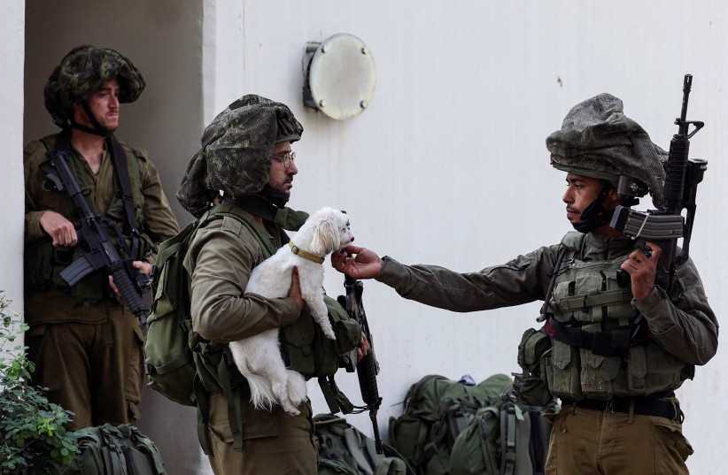  An Israeli soldier pets a rescued dog near a bomb shelter in Kibbutz Kfar Aza, in southern Israel, October 10, 2023.  (credit: RONEN ZVULUN/REUTERS)