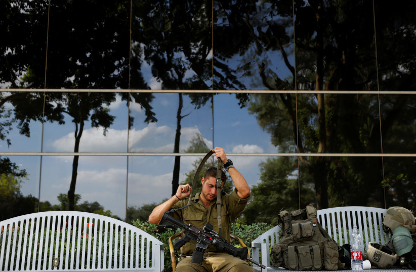  An Israeli soldier arranges his gun on a bench following a mass infiltration by Hamas gunmen from the Gaza Strip, in Kibbutz Beeri in southern Israel, October 13, 2023. (credit: REUTERS/AMIR COHEN)