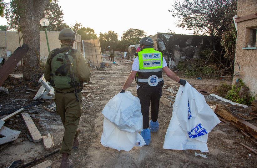  Members of Zaka walk through the destruction caused by Hamas Militants in Kibbutz Kfar Aza, as they collect the dead bodies, near the Israeli-Gaza border, in southern Israel, October 15, 2023.  (credit: EDI ISRAEL/FLASH90)