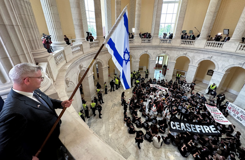  Rep. Brandon Williams (R-NY) dangles an Israeli flag over protesters, many of whom said they are Jewish, as they hold a civil disobedience action calling for a cease fire in Gaza and an end to the Israel-Hamas conflict while occupying the rotunda of the Cannon House office building on Capitol Hill. (credit: JONATHAN ERNST/REUTERS)