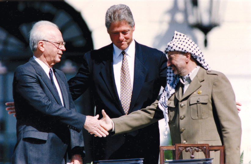  PLO chairman Yasser Arafat shakes hands with Israeli prime minister Yitzhak Rabin as US president Bill Clinton stands between them, after the signing of the Oslo Peace Accords at the White House on September 13, 1993. (credit: GARY HERSHORN/REUTERS)