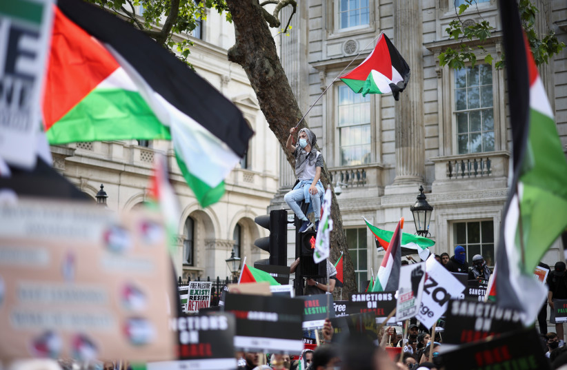  A protester holds a flag as he sits on a traffic light post during a pro-Palestine demonstration outside Downing Street in London, Britain, June 12, 2021 (credit: REUTERS/HENRY NICHOLLS)