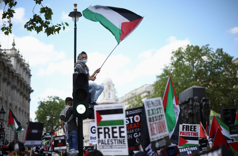  A protester holds a flag as he sits on a traffic light post during a (different, years earlier) pro-Palestine demonstration outside Downing Street in London, Britain, June 12, 2021. (credit: REUTERS/HENRY NICHOLLS)