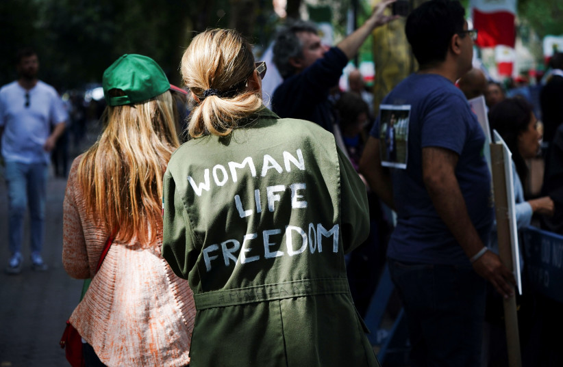  A woman wearing a jacket painted with the slogan ''Woman Life Freedom'' walks past a demonstration by supporters of the Mujahideen-e-Khalq (MEK), an Iranian dissident group, near the United Nations headquarters during the visit of Iran's President Ebrahim Raisi in New York, September 19, 2023. (credit: REUTERS/BING GUAN)