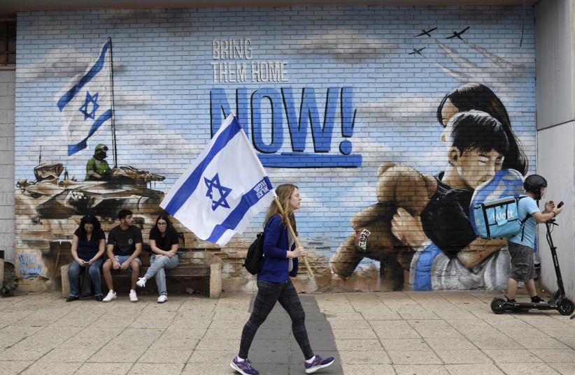  An Israeli woman carries an Israeli flag as she passes in front of a graffity calling for the release of Israelis held hostage by Hamas in Gaza, on November 12, 2023 (credit: GILI YAARI /FLASH90)