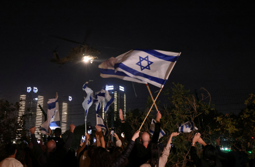 People wave Israeli flags as a helicopter, carrying hostages, departs from Schneider Children's Medical Center in Petah Tikva, Israel, November 24, 2023 (credit: RONEN ZVULUN/REUTERS)