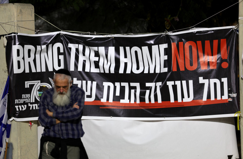  A man stands next to a banner as hostages are expected to be released by the Palestinian militant group Hamas, amid a hostages-prisoners swap deal between Hamas and Israel, in Tel Aviv, Israel, November 26, 2023 (credit: REUTERS/ATHIT PERAWONGMETHA)