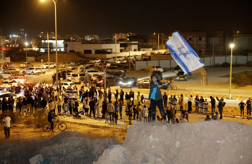 A boy waves an Israeli flag, as people wait for an expected convoy carrying newly released hostages that were seized during the October 7 attack by Palestinian militant group Hamas and held in the Gaza Strip, in Ofakim, Israel, November 26, 2023 (credit: REUTERS/AMIR COHEN)
