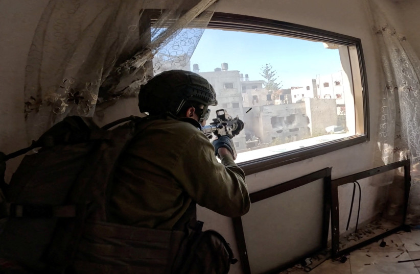  An Israeli soldier fires a weapon from a window during operations in the Gaza Strip amid the ongoing conflict between Israel and the Palestinian Islamist group Hamas, in this screen grab taken from a handout video released on December 4, 2023. (credit: REUTERS/IDF HANDOUT)
