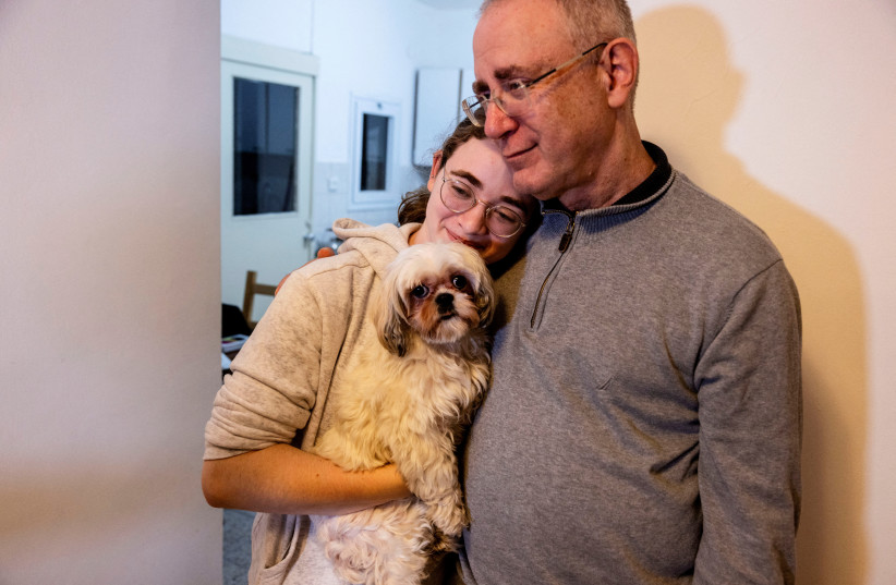  Mia Leimberg, 17, released from captivity after being taken hostage by Hamas in the Gaza Strip with her mother Gabriela and her dog Bella, holds the dog in her arms as she rests her head on the shoulder of her father, Moshe, at their home in Jerusalem, December 5, 2023. (credit: REUTERS/Ronen Zvulun)