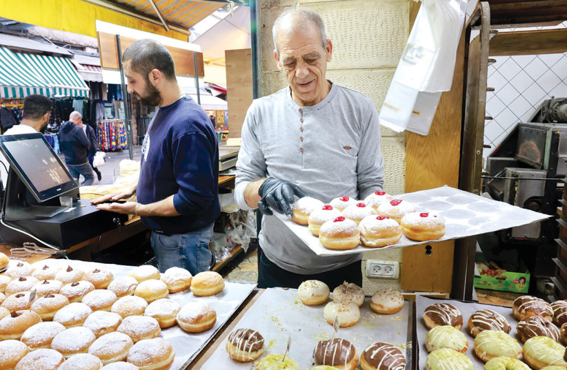  Workers set up Hanukkah doughnuts, including sufganiyot, at Duvshanit in the Mahane Yehuda market. (credit: MARC ISRAEL SELLEM)