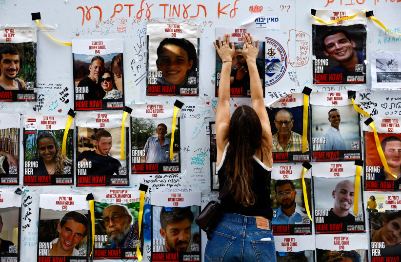  A woman puts up a poster on a message board with pictures of hostages, who are being held in the Gaza Strip after they were seized by Hamas gunmen on October 7, amid the ongoing conflict between Israel and the Palestinian Islamist group Hamas, in Tel Aviv, Israel December 6, 2023. (credit: REUTERS/CLODAGH KILCOYNE)