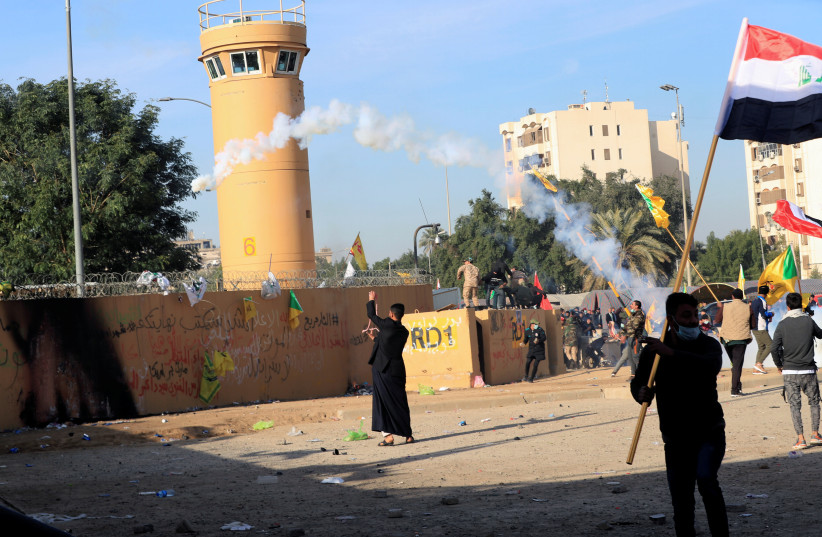 Protesters and militia fighters throw back a tear gas canister used by U.S. Embassy security men during a protest to condemn air strikes on bases belonging to Hashd al-Shaabi (paramilitary forces), outside the embassy in Baghdad, Iraq January 1, 2020. (credit: THAIER AL-SUDANI/REUTERS)