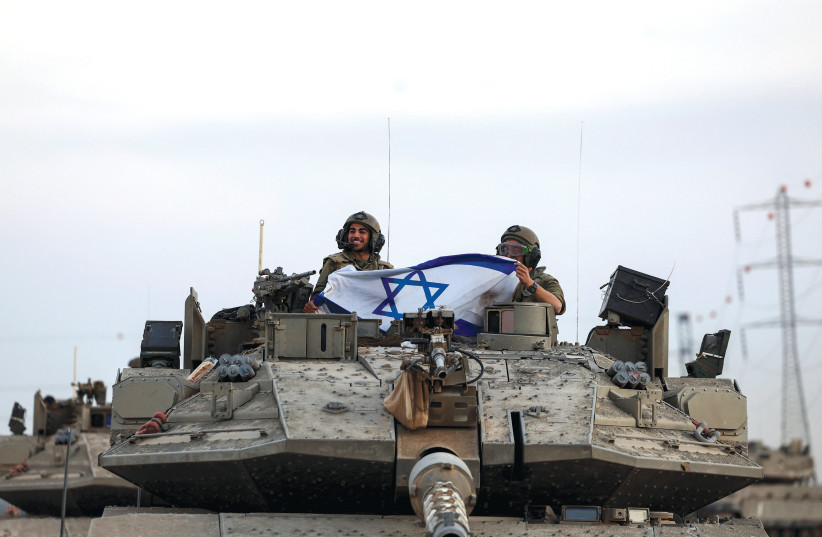  Israeli soldiers in a tank hold an Israeli flag near Israel's border with the Gaza Strip (credit: RONEN ZVULUN/REUTERS)