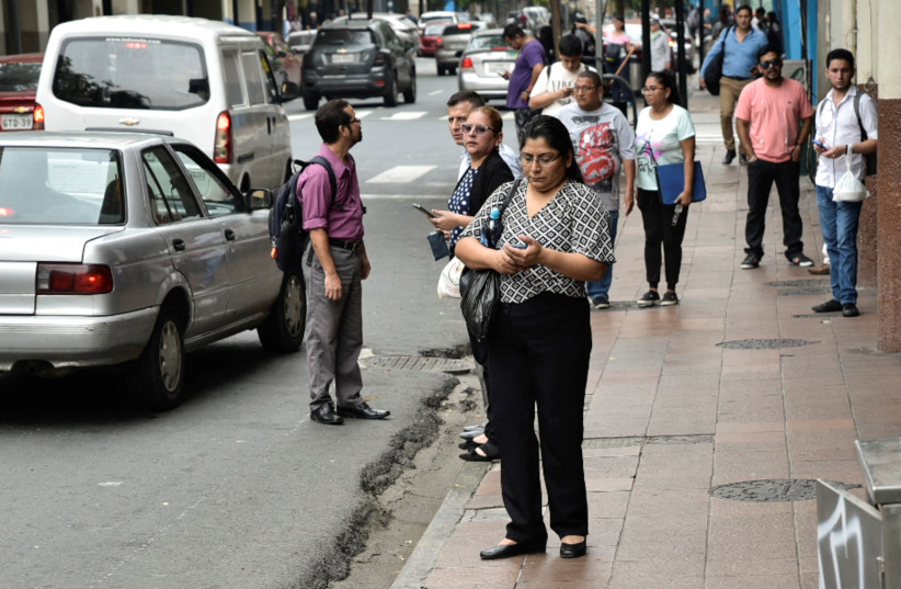  A woman uses a cellphone as people stand on a sidewalk after a violence outbreak a day after Ecuador's President Daniel Noboa declared a 60-day state of emergency following the disappearance of Adolfo Macias. (credit: REUTERS/VICENTE GAIBOR DEL PINO)
