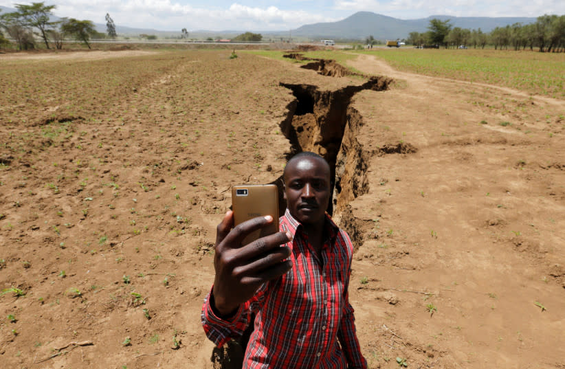  Un hombre se toma una foto selfie cerca de una sima que se sospecha ha sido causada por un fuerte aguacero a lo largo de una falla subterránea cerca de la ciudad de Mai Mahiu, en el Valle del Rift. (credit: REUTERS)