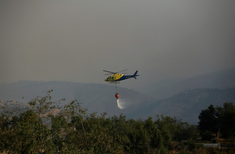  A helicopter flying over a burnt area drops water from a bucket to douse flames during the spread of wildfires in Vina del Mar, Chile February 3, 2024. (credit: REUTERS/SOFIA YANJARI)