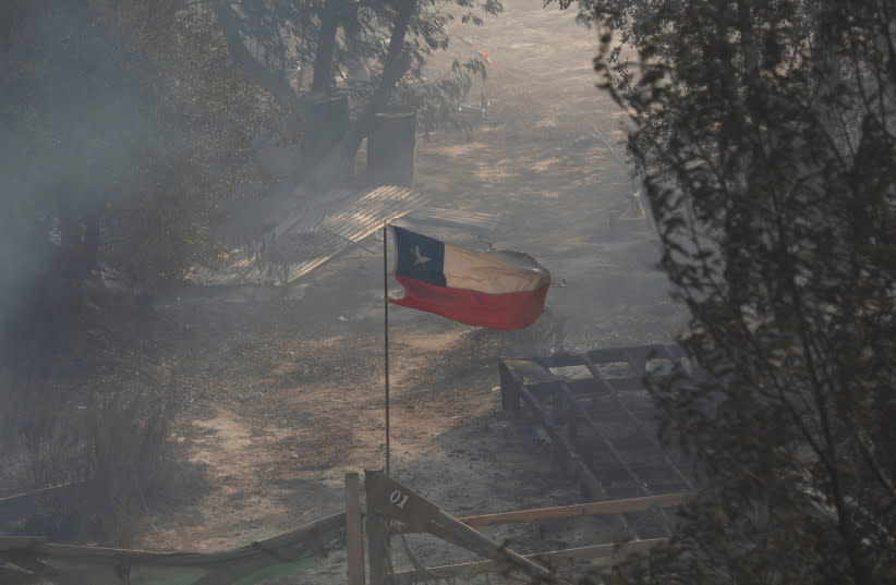  La bandera nacional de Chile ondea entre el humo y cerca de los restos quemados de una casa tras la propagación de los incendios forestales, en Viña del Mar, Chile 3 de febrero de 2024. (credit: REUTERS/SOFIA YANJARI)