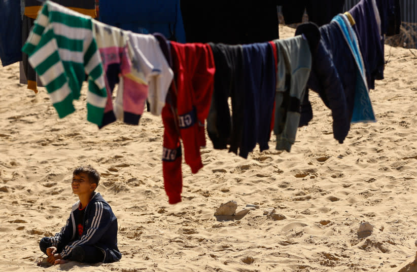  Un niño sentado junto a ropa colgada, mientras los palestinos desplazados, que huyeron de sus casas debido a los ataques israelíes, se refugian en la frontera con Egipto, en Rafah, en el sur de la Franja de Gaza, 8 de febrero de 2024. (credit: REUTERS/IBRAHEEM ABU MUSTAFA)