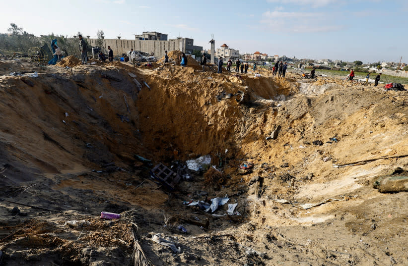  Palestinos se reúnen cerca de un cráter en el lugar de un ataque israelí contra una casa en Rafah, en el sur de la Franja de Gaza, 18 de febrero de 2024. (credit: REUTERS/MOHAMMED SALEM)